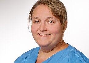 Stefanie Reiß Kopf-und-Schulter-Porträt einer lächelnden Person in blauer medizinischer Kleidung vor neutralem Hintergrund.