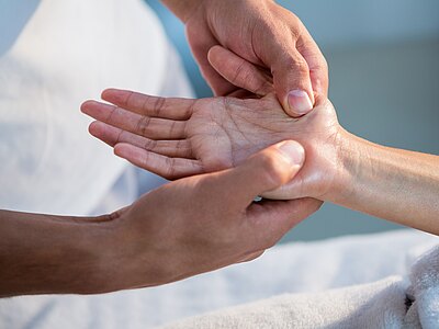 Großaufnahme: Eine Person übt mit dem Daumen Druck auf die offene Handfläche einer anderen Person aus – eine Handmassage/Reflexzonenbehandlung zur Entspannung.